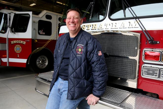 Jeff Denton smiling while sitting on the front of a fire truck. 